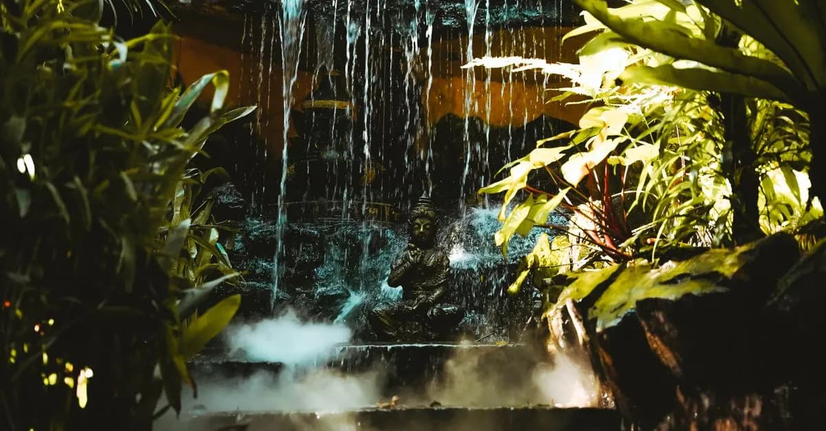 A serene Buddha statue surrounded by lush foliage and a cascading waterfall in Bangkok, Thailand.