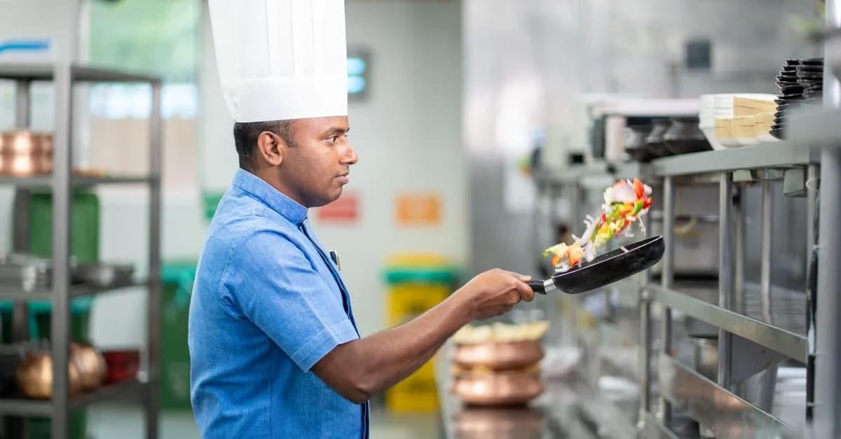 Professional chef tossing a pan of vegetables in a commercial kitchen, showcasing culinary skills.