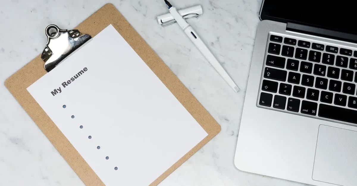 A clipboard with a resume beside a pen and laptop on a marble desk, ideal for business and job application themes.