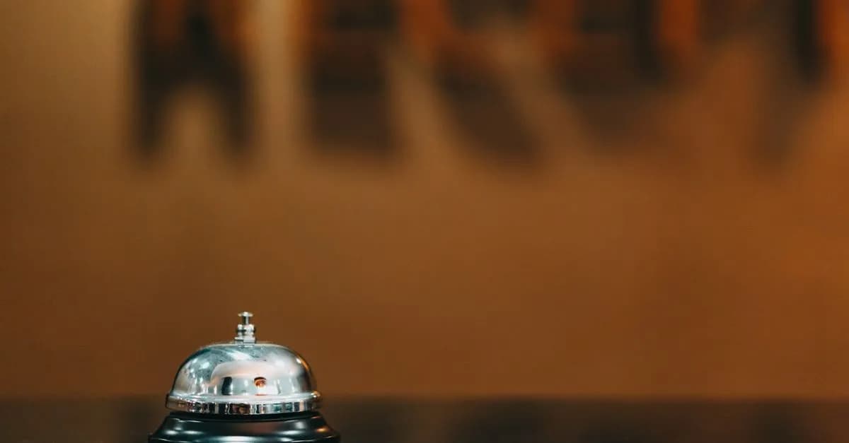 Close-up image of a silver hotel bell on a black surface with 'RECEPTION' blurred in the background.