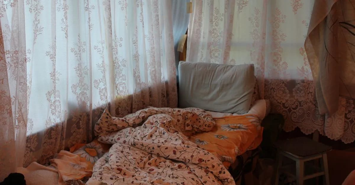 Warm and inviting bedroom featuring lace curtains and a tousled bed. Ideal for cozy home concepts.
