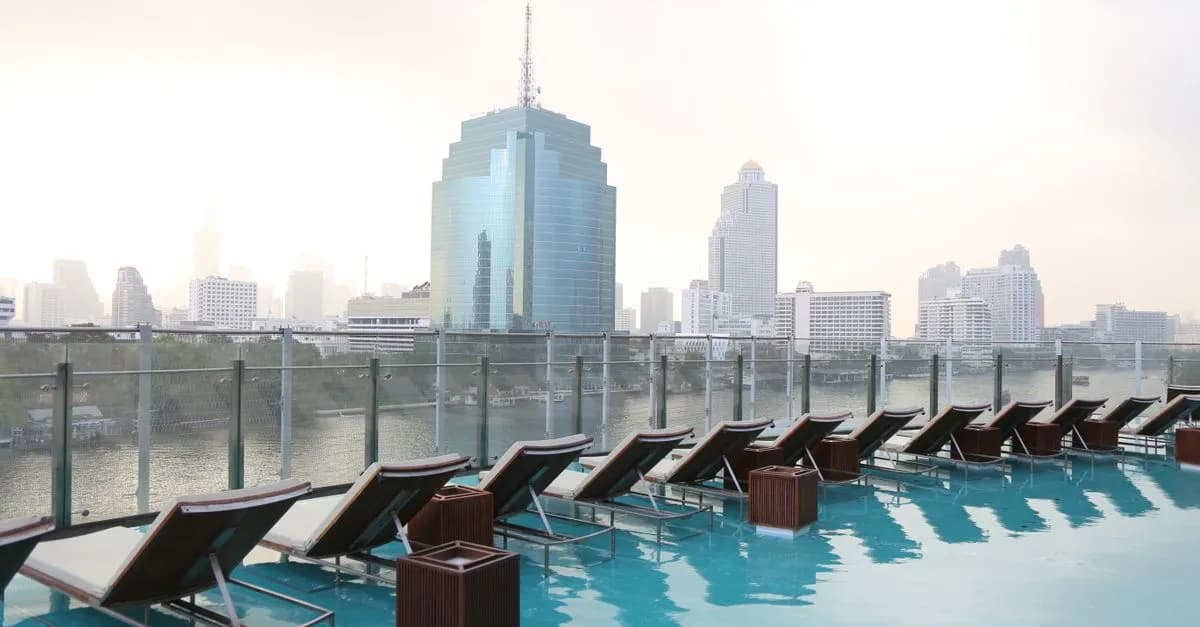 Serene rooftop pool with Bangkok's modern skyline and river view at sunrise.