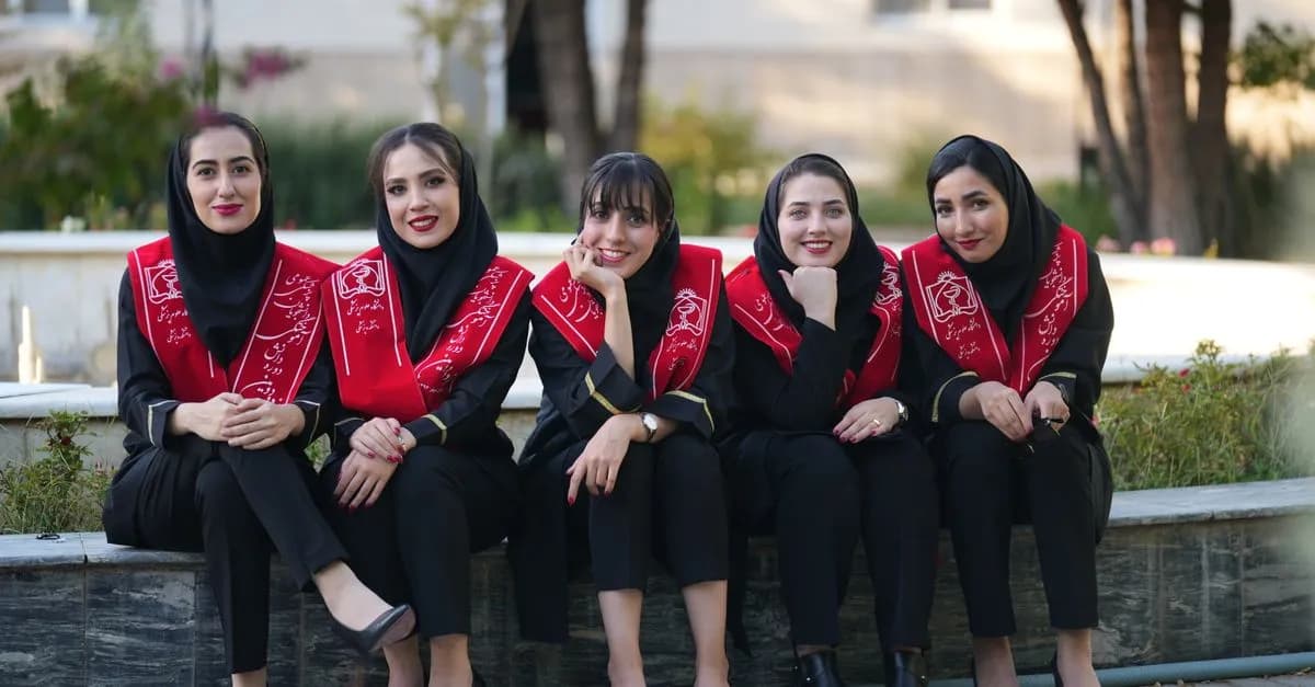 Five Iranian women in graduation attire, smiling outdoors, celebrate their achievement together.