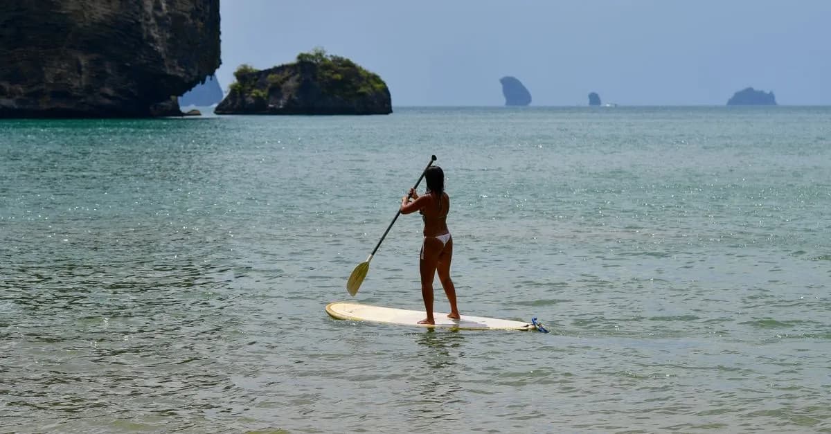 Woman paddleboarding by limestone cliffs in Krabi, Thailand. Perfect summer escape.